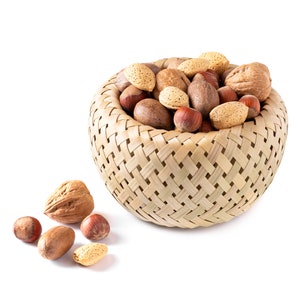 May include: A woven basket filled with a variety of nuts, including almonds, pecans, hazelnuts, and walnuts. Some nuts are scattered on a white surface.