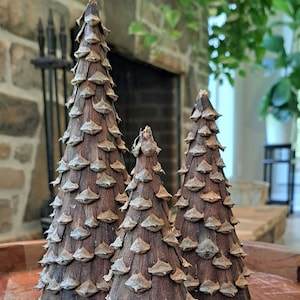 May include: Three brown pine cone Christmas trees of varying sizes on a wooden surface.