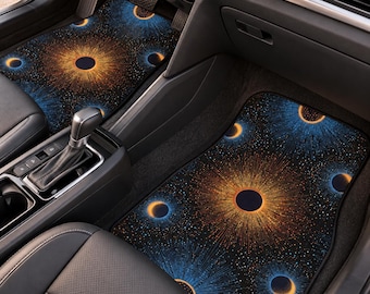May include: A pair of car floor mats featuring a black background with a vibrant celestial pattern of radiating orange and blue light bursts and dark circular silhouettes, installed in the front footwells of a vehicle interior.