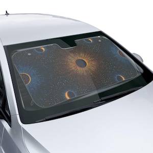 May include: Car windshield sunshade with a dark background and a colorful abstract design. The design features circular patterns in shades of blue, orange, and yellow, with a central dark circle. The sunshade is installed in a white car.