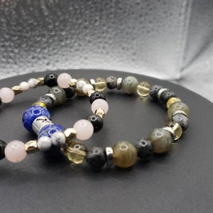 May include: Two beaded bracelets featuring a variety of coloured stones, including black, white, pink, yellow and grey. One bracelet has a blue stone with a silver charm.