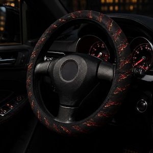 May include: A black steering wheel cover featuring a vibrant, fiery orange and red lightning-like pattern. The cover is fitted onto a standard circular steering wheel inside a vehicle, showcasing a textured design that contrasts with the dark interior.