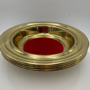 May include: A gold-colored ashtray with a circular design. The ashtray has a red velvet center and three small grooves for resting cigarettes. The exterior has a ridged pattern.