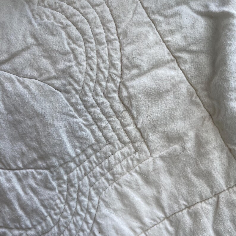 Peut inclure: Un tissu matelass&eacute; blanc pr&eacute;sentant une s&eacute;rie de lignes cousues parall&egrave;les et incurv&eacute;es qui cr&eacute;ent un motif textur&eacute; en forme de vagues sur toute la surface. Le mat&eacute;riau semble doux et mat, avec des d&eacute;tails de couture visibles partout.