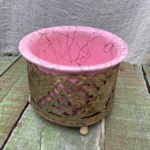May include: A pink ceramic planter with a gold metal stand. The planter has a crackled glaze and the stand has a floral design.