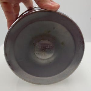 May include: A close-up of the base of a stainless steel Stanley vacuum flask. The base is a dark grey colour with a circular indentation. The Stanley logo is visible in the centre, with text that reads "Stanley Insulating Co. New Britain, Conn. U.S.A."