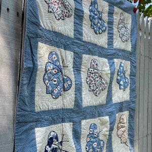 Peut inclure: Un quilt en patchwork compos&eacute; d'une grille de carr&eacute;s en tissu blanc cass&eacute;, chacun pr&eacute;sentant une applique de papillon unique faite de divers tissus &agrave; motifs bleus, blancs et floraux. Les carr&eacute;s sont s&eacute;par&eacute;s par des bordures en tissu textur&eacute;.