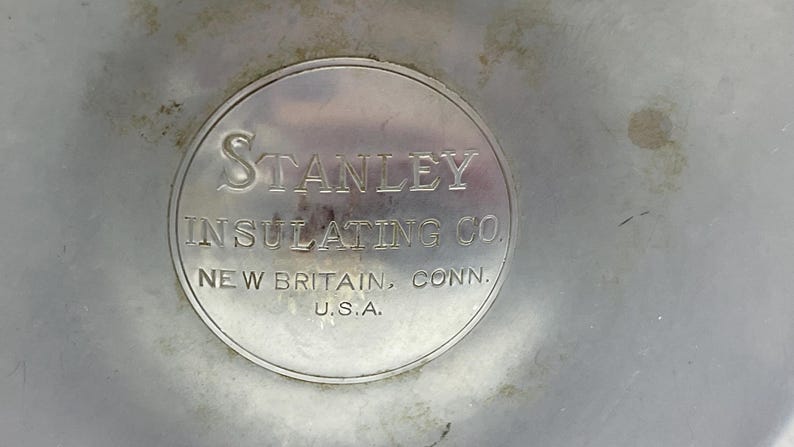 May include: A close-up of a metal object with the text "STANLEY INSULATING CO." in a circular emblem. The text "NEW BRITAIN, CONN. U.S.A." is also visible. The object has a silver finish.