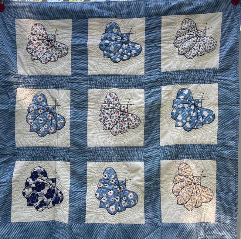 Peut inclure: Une courtepointe carr&eacute;e compos&eacute;e d'une grille de neuf blocs de tissu blanc, chacun pr&eacute;sentant une applique de papillon en tissu en trois dimensions. Les papillons sont faits de divers tissus bleus, blancs et &agrave; motifs floraux. Bordure bleue.