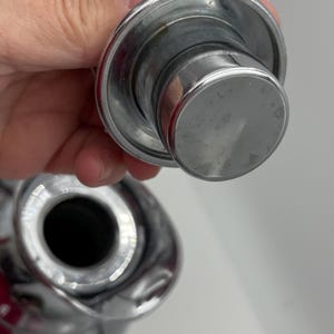 May include: Close-up of a shiny, chrome bottle stopper. The stopper has a circular top and a cylindrical body. The image is well-lit, highlighting the metallic sheen of the product. The stopper appears to be new and unused.