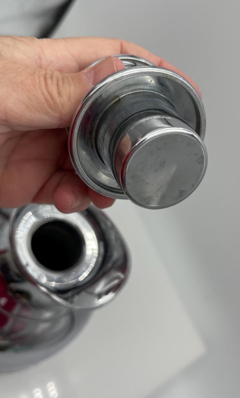 May include: Close-up of a shiny, chrome bottle stopper. The stopper has a circular top and a cylindrical body. The image is well-lit, highlighting the metallic sheen of the product. The stopper appears to be new and unused.