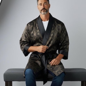May include: A black and gold patterned robe with a black satin collar and cuffs. The robe is tied at the waist with a black sash. The model is wearing a white shirt and blue jeans.