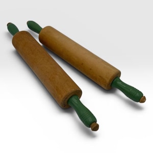 May include: Two wooden rolling pins with natural brown cylindrical barrels and green painted handles. Each rolling pin features a central rotating barrel and two green handles with ribbed detailing at the ends, positioned diagonally.