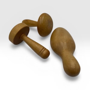 May include: Three wooden kitchen tools are displayed against a white background. The tools include a small mallet, a scoop, and a mushroom-shaped tool. The wood has a warm, light brown tone. The tools appear to be new.