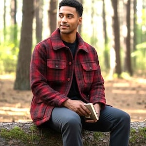 May include: A red and black plaid button-up jacket with a collar, long sleeves, and two chest pockets with flaps. The jacket is worn over a plain black shirt, paired with dark gray trousers, and is held together by dark buttons down the front.
