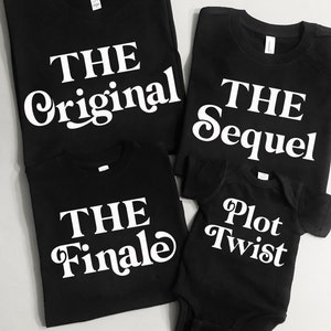 May include: Four black t-shirts and a onesie with white text. The shirts read "THE Original", "THE Sequel", "THE Finale", and the onesie says "Plot Twist". The shirts are folded and arranged on a light gray surface.