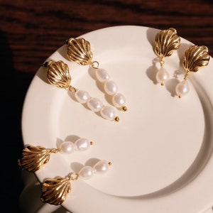 May include: Three pairs of gold shell-shaped earrings with pearl drops. Each pair features a different length of pearl drops.