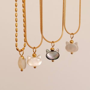 May include: Three gold chain necklaces with cat-shaped pendants. The pendants are made of white and gray mother-of-pearl.