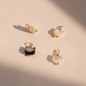 May include: Four small cat-shaped charms made of white and black mother of pearl with gold accents.