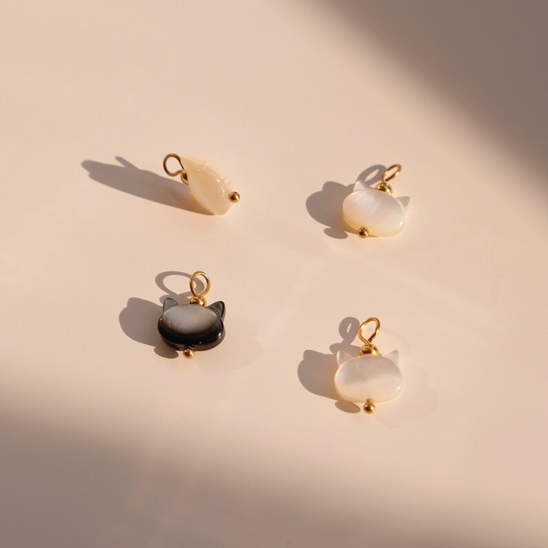 May include: Four small cat-shaped charms made of white and black mother of pearl with gold accents.