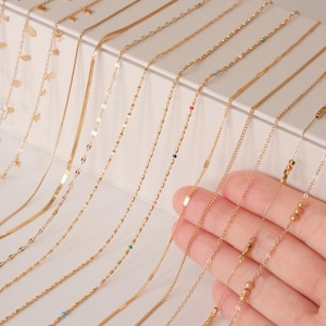 K&ouml;nnte beinhalten: Eine Sammlung von goldenen Kettenhalsketten mit verschiedenen Stilen und Verzierungen, darunter Perlen, Quadrate und kleine farbige Steine.