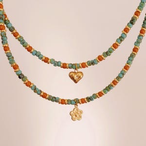 May include: A layered necklace with turquoise and orange beads. The necklace features a gold heart charm and a gold flower charm.