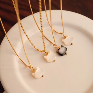 May include: Four gold necklaces with cat-shaped pendants. Three pendants are white and one is black.