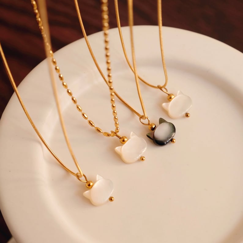 May include: Four gold necklaces with cat-shaped pendants. Three pendants are white and one is black.