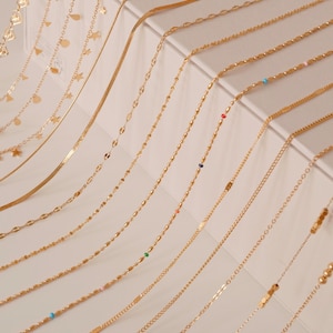 K&ouml;nnte beinhalten: Eine Sammlung von 15 goldenen Ketten in verschiedenen L&auml;ngen und Stilen, darunter Ketten mit kleinen Anh&auml;ngern, Perlen und einer einfachen Schlangenkette.