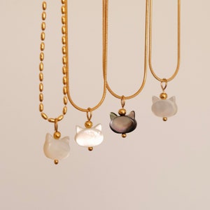 May include: Three gold chain necklaces with cat-shaped pendants. The pendants are made of white and black mother-of-pearl.