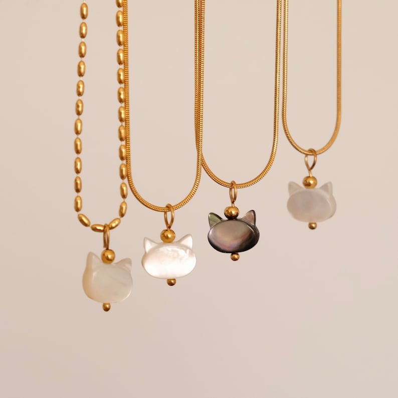 May include: Three gold chain necklaces with cat-shaped pendants. The pendants are made of white and black mother-of-pearl.
