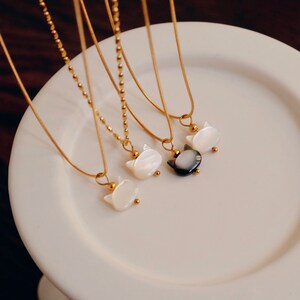 May include: Four gold chain necklaces with cat-shaped pendants. The pendants are made of white and black mother-of-pearl.