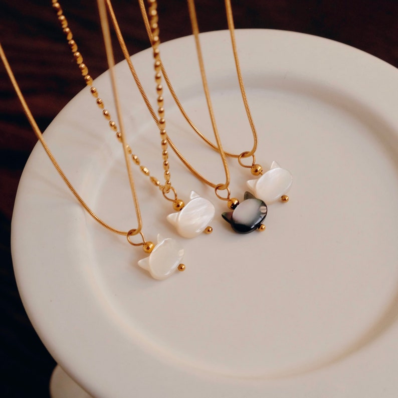 May include: Four gold chain necklaces with cat-shaped pendants. The pendants are made of white and black mother-of-pearl.