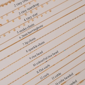 K&ouml;nnte beinhalten: Nahaufnahme von 15 verschiedenen goldenen Ketten, jede mit einem einzigartigen Stil und Design. Die Ketten sind mit Nummern und Namen beschriftet, wie z. B. Herz-Kette, kleines Dreieck, kleine Tr&auml;ne, kleiner Stern, Schlangen-Kette, 2 mm Fischgr&auml;t, Lippen-Kette, funkelnde Kette, Reiskette, bunte Reiskette, flache Bord&uuml;re, Bord&uuml;re, Kabel, W&uuml;rfelkette und Kugelkette.