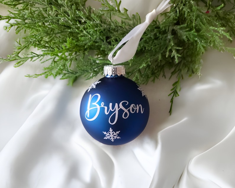 May include: Blue Christmas ornament with white snowflakes and the name "Bryson" written in white cursive.