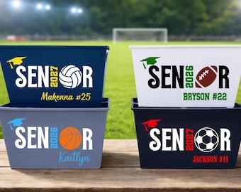 May include: Four rectangular storage bins in navy, white, gray, and black, each featuring the word SENIOR with a graduation cap, a sports ball, and a graduation year. Custom names and jersey numbers are printed in various colors on each bin.