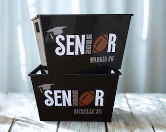 May include: Two black plastic storage bins stacked vertically. Each bin features white text reading SENIOR, a brown football graphic replacing the letter I, the year 2025, a white graduation cap icon, and personalized names Markia #6 and Rickelle #5.