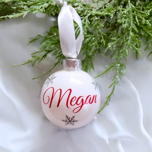 May include: White Christmas ornament with a red name "Megan" and silver snowflakes.