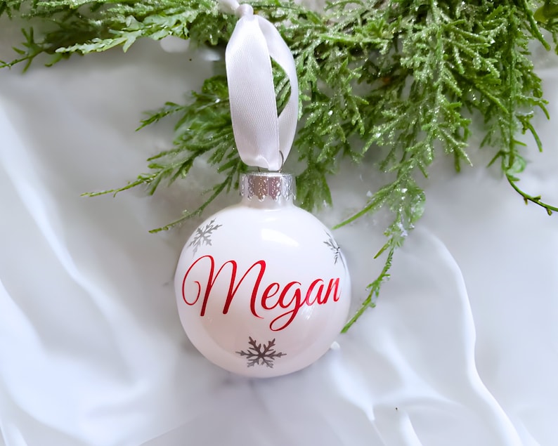 May include: White Christmas ornament with a red name "Megan" and silver snowflakes.