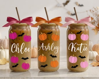 May include: Three glass tumblers filled with iced coffee, each featuring a bamboo lid, a metal straw, and a colorful ribbon bow. The glasses are decorated with pumpkin and bat graphics and the names Chloe, Ashley, and Katie in white script.