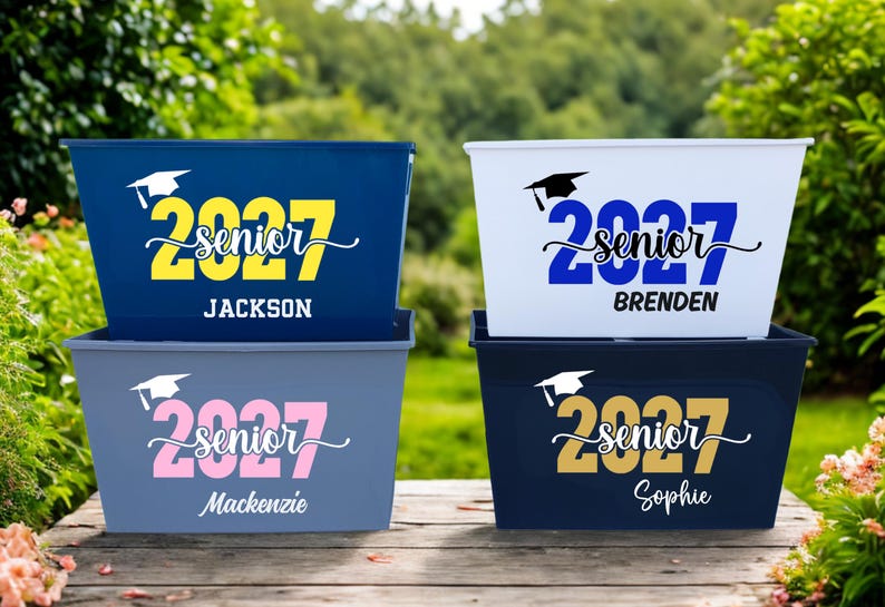 May include: Four rectangular storage bins in navy, white, light blue, and dark blue. Each bin features a graduation cap icon, the year 2027, the word senior in script, and a personalized name: Jackson, Brenden, Mackenzie, or Sophie in various colors.