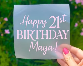 May include: A square, semi-transparent decal featuring light pink text that reads Happy 21st BIRTHDAY Maya! The lettering combines a cursive script for the words Happy and Maya with a bold, capitalized serif font for the word BIRTHDAY.