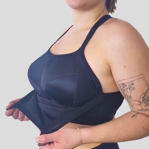 Op de afbeelding: Een zwarte sportbeha met verstelbare bandjes en een racerback-ontwerp. De beha heeft een ingebouwde shelf-beha en is ontworpen voor activiteiten met hoge impact.