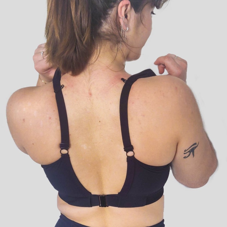 Op de afbeelding: Een zwarte sportbeha met verstelbare bandjes en een racerback-ontwerp. De beha heeft een haak- en oogsluiting aan de achterkant.