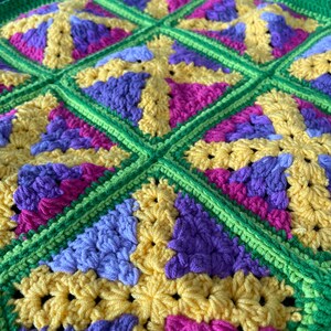 May include: A close-up of a crocheted blanket with a repeating pattern of yellow, green, purple, and pink squares.