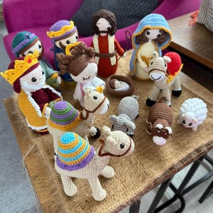Könnte beinhalten: Eine Weihnachtskrippe mit gehäkelten Figuren, darunter die drei Weisen aus dem Morgenland, Maria, Josef, das Jesuskind und Tiere. Die Figuren sind aus Garn in verschiedenen Farben gefertigt, darunter Rot, Blau, Gelb und Grün.
