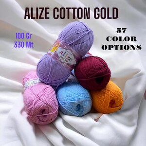 May include: A close-up of six balls of yarn in various colours, including purple, pink, blue, red, and orange. The yarn is labelled "Alize Cotton Gold" and is 100 grams and 330 metres long. There are 57 colour options available.