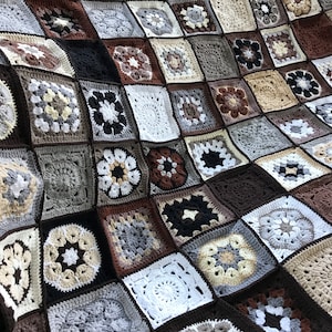 May include: A crocheted blanket made of squares in various shades of brown, gray, and white. The squares are arranged in a grid pattern and feature different floral designs.