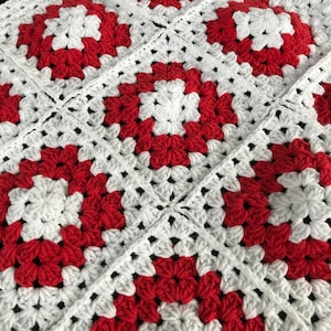 Op de afbeelding: Een rood-wit gehaakt deken met een granny square patroon.