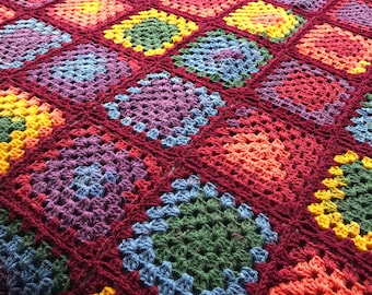 May include: A colorful crocheted blanket with a variety of squares in different colors, including red, purple, green, blue, and yellow.